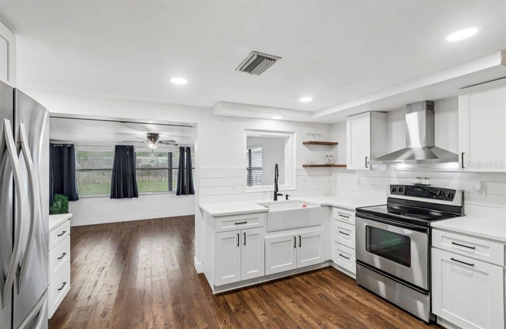 A white kitchen features a farmhouse sink, stainless steel appliances, and wood-look flooring — 4531 KENNEDY DRIVE, NEW PORT RICHEY, FL