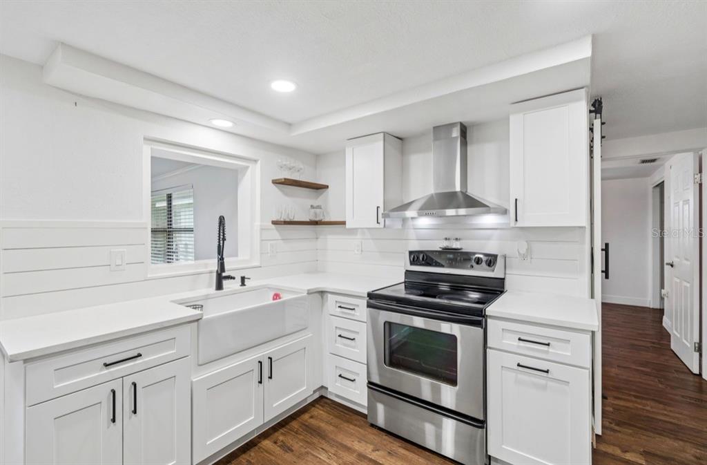 A white kitchen features a farmhouse sink, stainless steel appliances, and wood-look flooring — 4531 KENNEDY DRIVE, NEW PORT RICHEY, FL