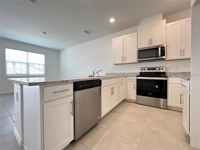 A modern kitchen features white cabinets, stainless steel appliances, and a granite-topped island — 2343 GARDEN  BELLE DRIVE, CLERMONT, FL