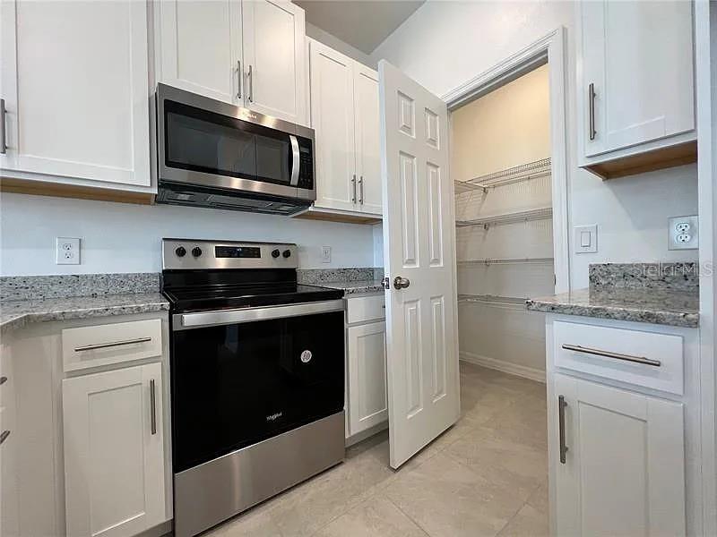 A kitchen features white cabinets, stainless steel appliances, granite countertops, and an open pantry door — 2343 GARDEN  BELLE DRIVE, CLERMONT, FL