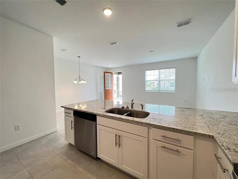 A kitchen features white cabinets, granite countertops, a stainless steel dishwasher, and tile flooring — 2343 GARDEN  BELLE DRIVE, CLERMONT, FL