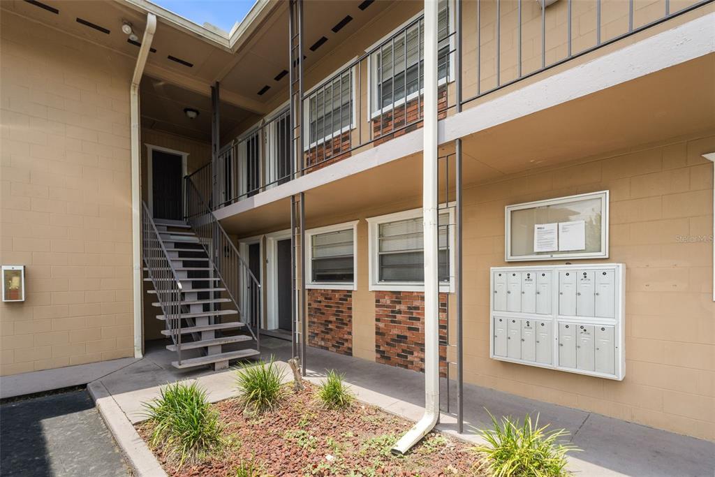 An exterior view of a two-story apartment building with stairs, mailboxes, and a small garden — 501 NW 15TH AVENUE UNIT 11, GAINESVILLE, FL