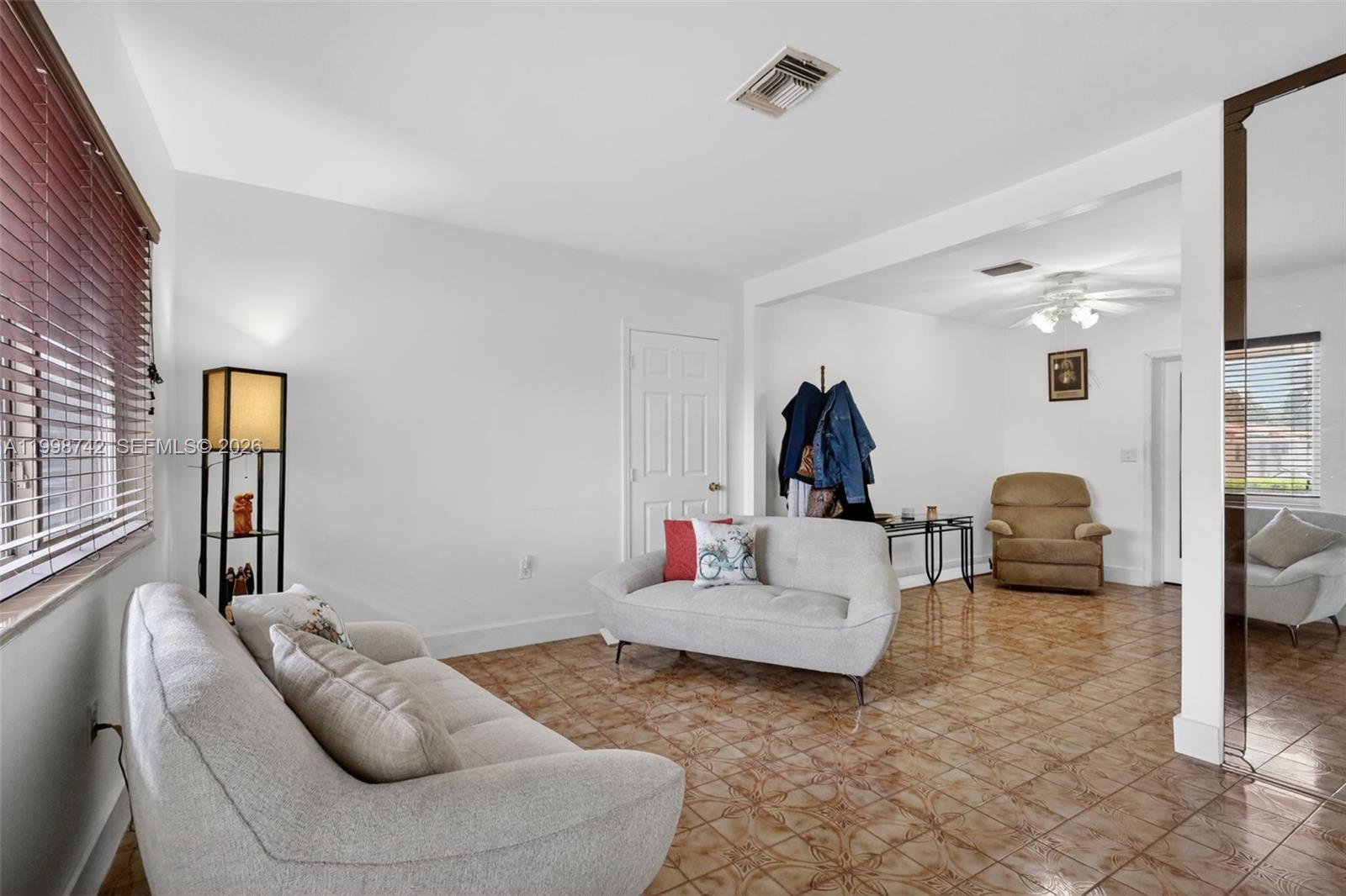 A living room features light-colored sofas, tiled flooring, and a coat rack near a doorway — 733 W 33rd St, Hialeah FL 33012, HIALEAH, FL