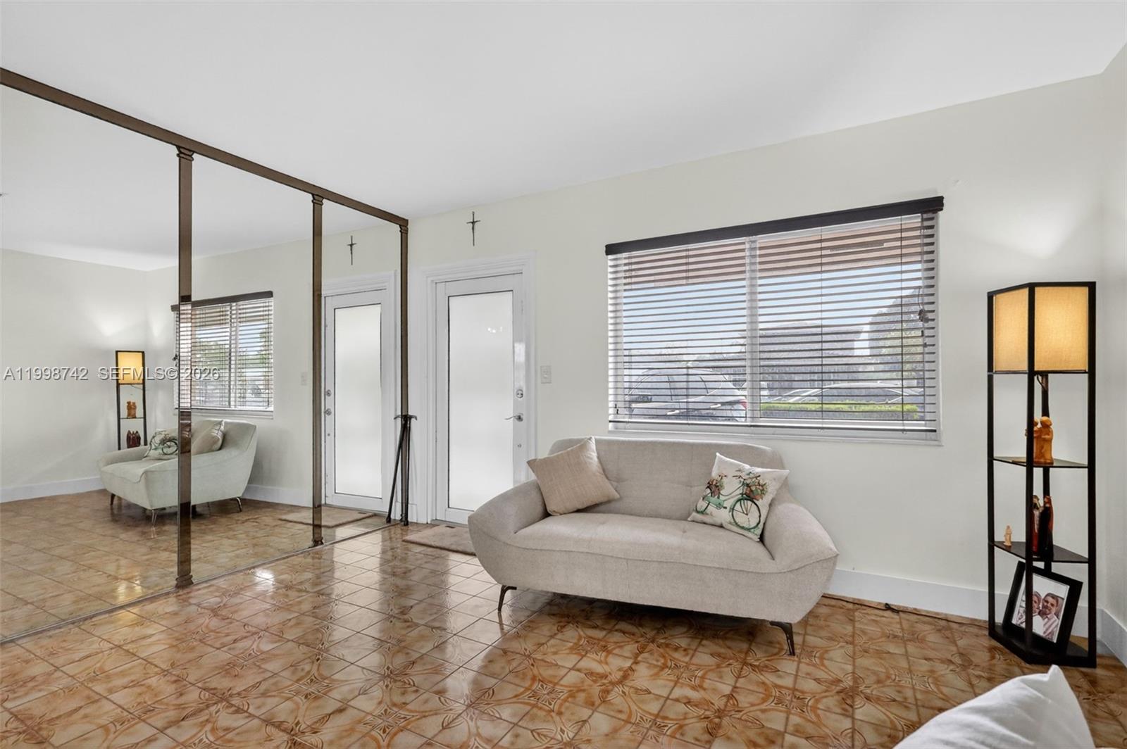 A living room features tiled floors, a mirrored wall, a sofa, and a floor lamp — 733 W 33rd St, Hialeah FL 33012, HIALEAH, FL
