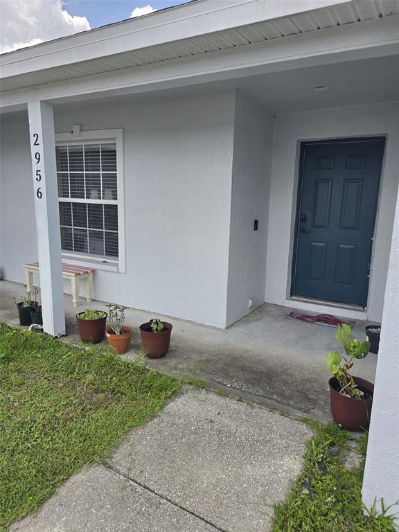 A covered concrete porch features a blue front door, a window, and several potted plants — 2956 COACH LAMP ROAD, MULBERRY, FL