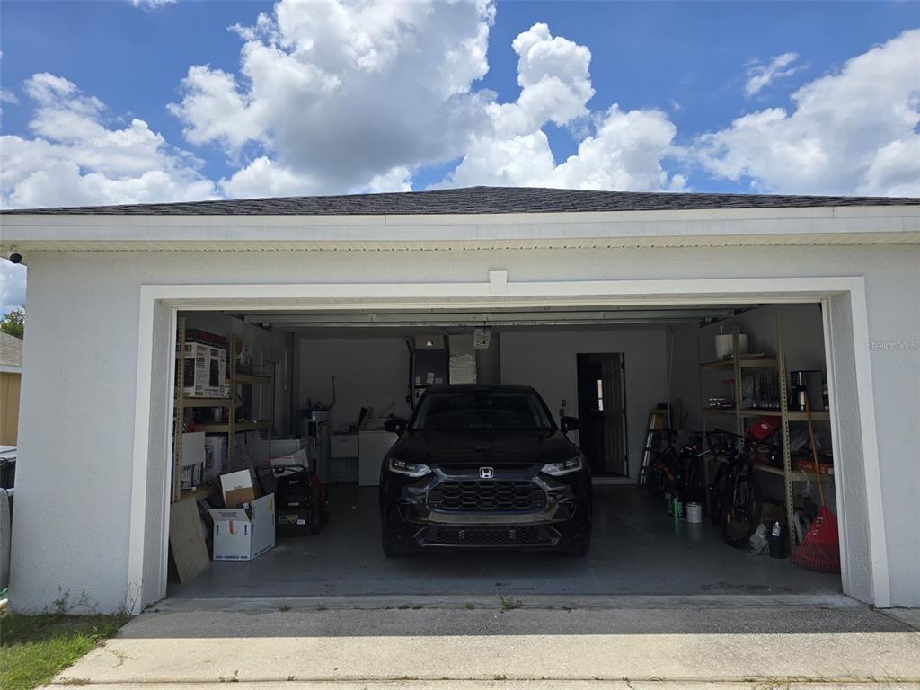 A black car is parked inside a residential garage with storage shelving on both sides — 2956 COACH LAMP ROAD, MULBERRY, FL