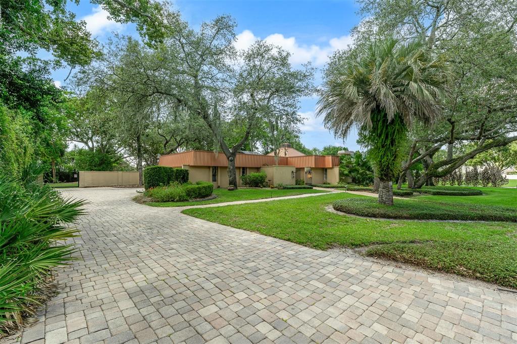 A paved driveway leads to a single-story house with a copper-colored roof among trees — 229 FLAME AVENUE, MAITLAND, FL