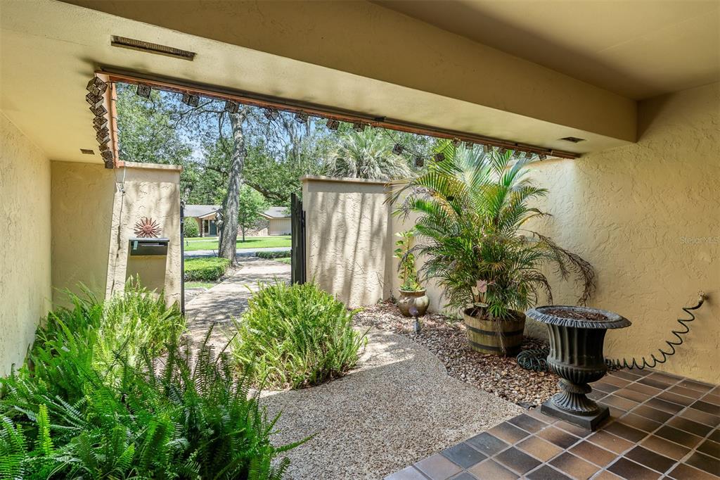 A covered entryway features a tiled floor, a gravel courtyard, potted plants, and a gate — 229 FLAME AVENUE, MAITLAND, FL