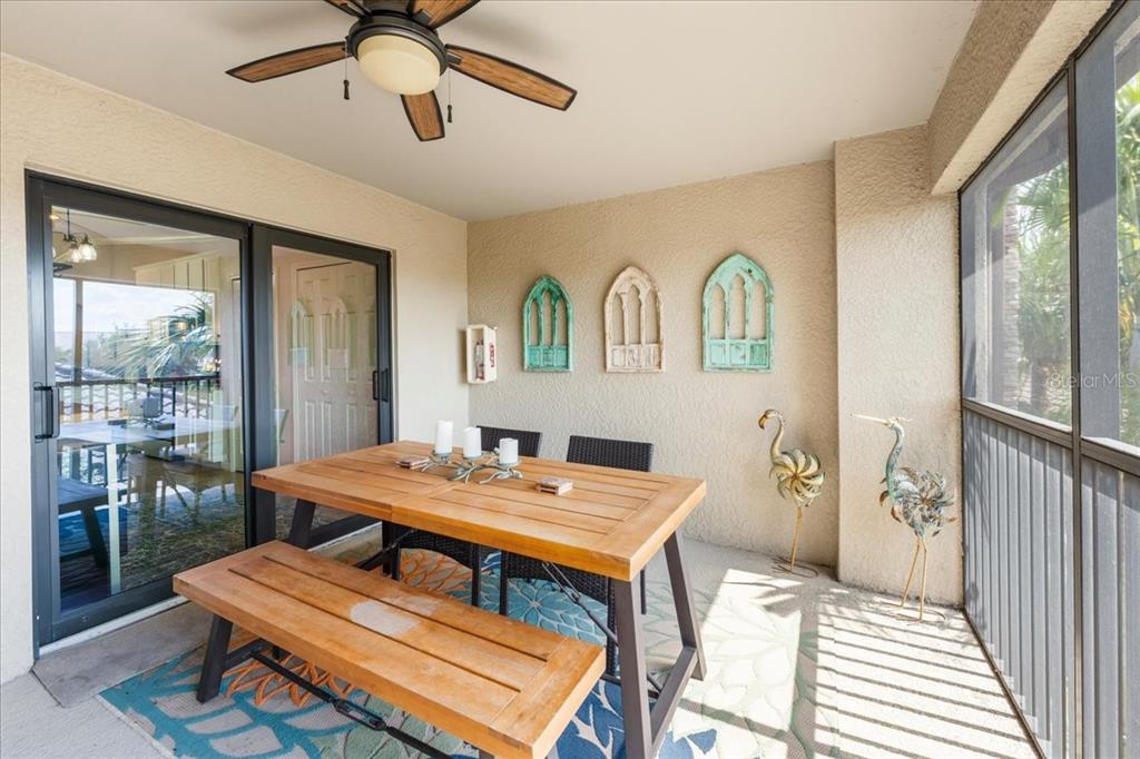 A screened-in patio features a wooden dining set, a ceiling fan, and wall decor — 5557 PALMER CIRCLE UNIT 202, BRADENTON, FL