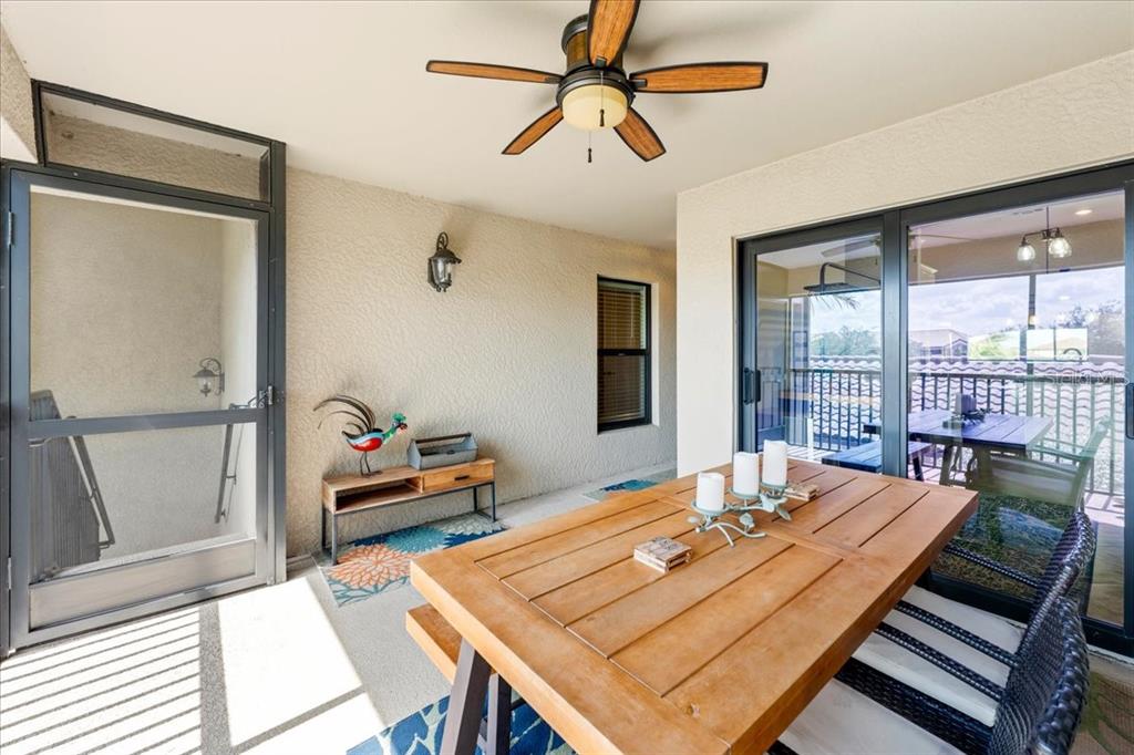 A covered patio features a wooden dining table, a ceiling fan, and a screen door — 5557 PALMER CIRCLE UNIT 202, BRADENTON, FL