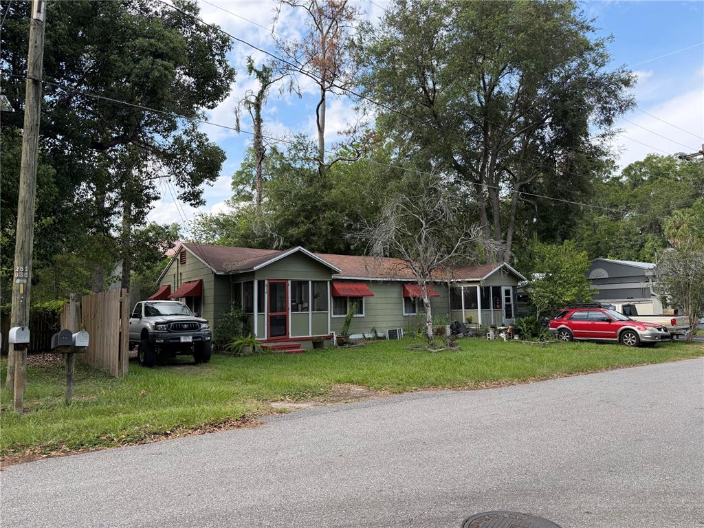 A single-story house with green siding, red awnings, and a screened porch sits on a lawn — 608 NW 24TH AVENUE, GAINESVILLE, FL
