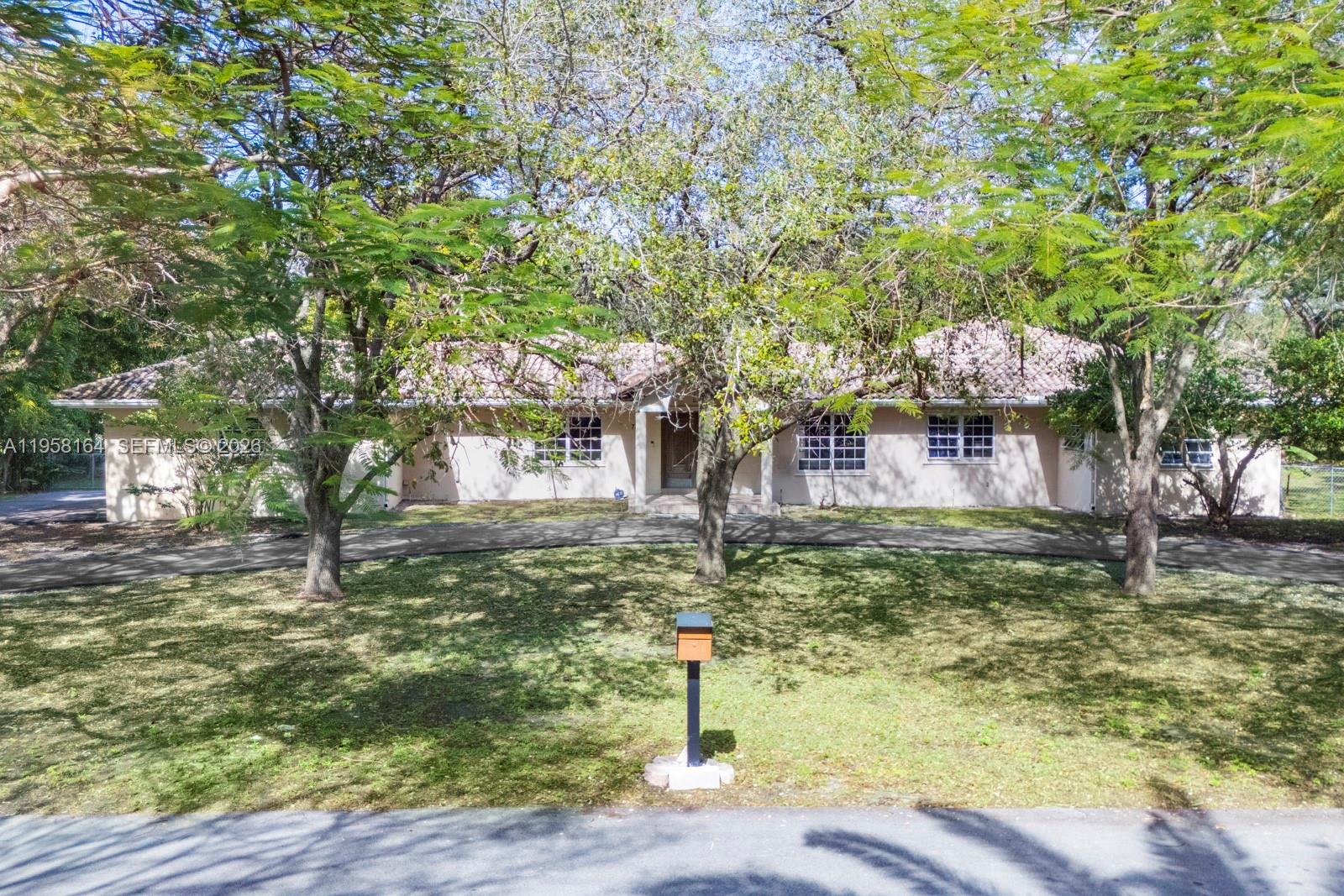 A single-story house with a tiled roof and a curved driveway sits behind mature trees — 7821 SW 129th Ter, Pinecrest FL 33156, PINECREST, FL