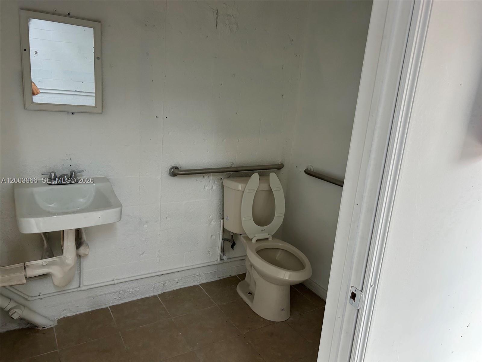 A small, utilitarian bathroom features a wall-mounted sink, a toilet with grab bars, and tile — 2776 NW 21st Ter, Miami FL 33142, MIAMI, FL