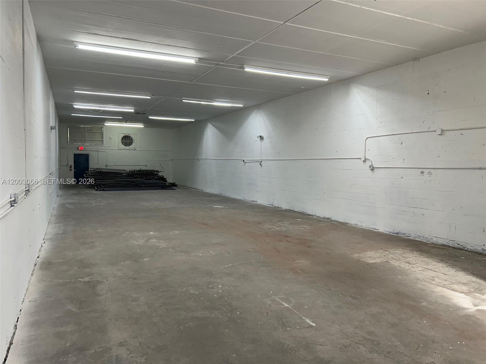 An empty, rectangular warehouse space features white concrete block walls, a concrete floor, and overhead lighting — 2776 NW 21st Ter, Miami FL 33142, MIAMI, FL