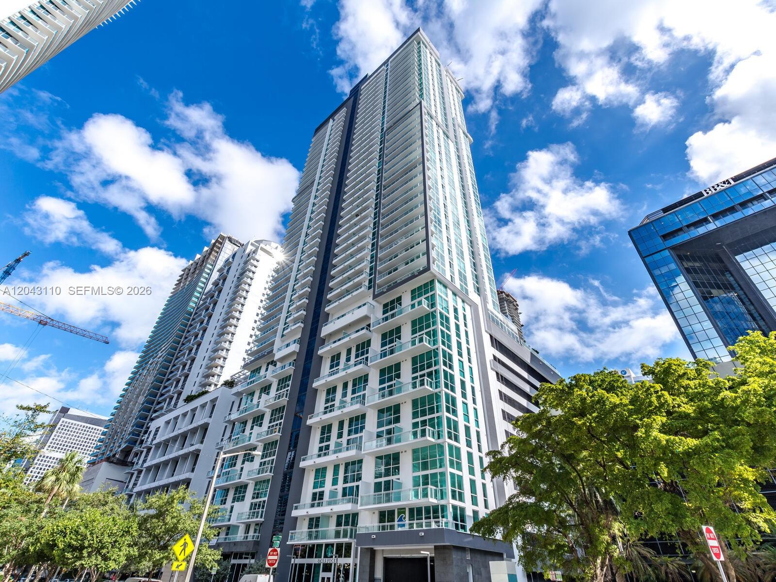 A balcony with a white sofa overlooks a city skyline with multiple high-rise buildings — 1080 Brickell Ave # 1509, Miami FL 33131, MIAMI, FL