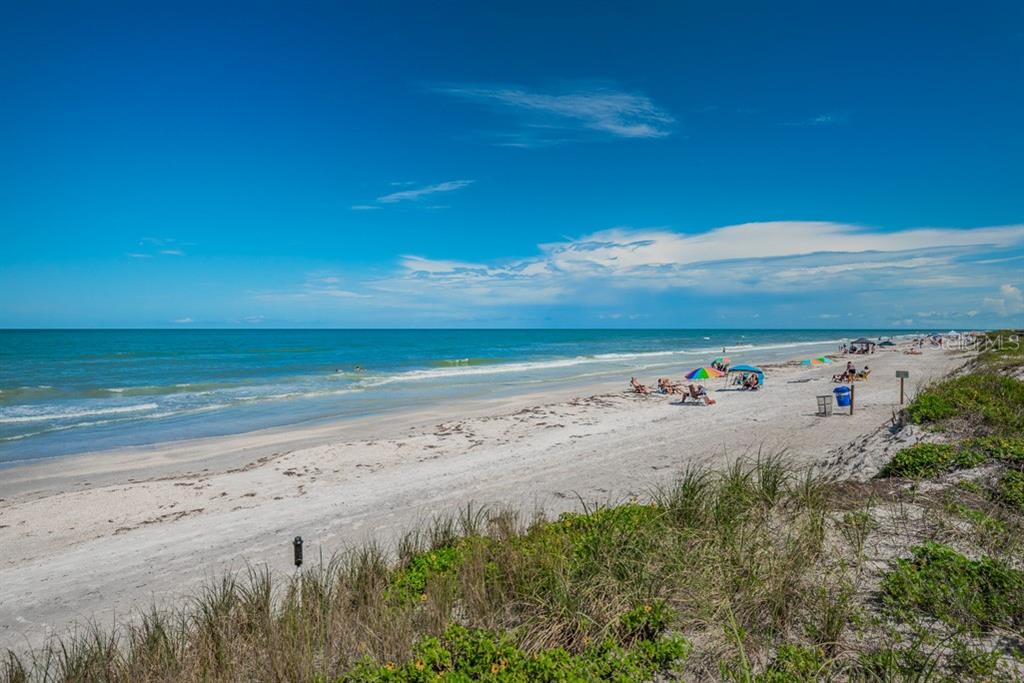 A sandy beach with dunes, ocean waves, and people under umbrellas under a blue sky — 372 12TH AVENUE, INDIAN ROCKS BEACH, FL