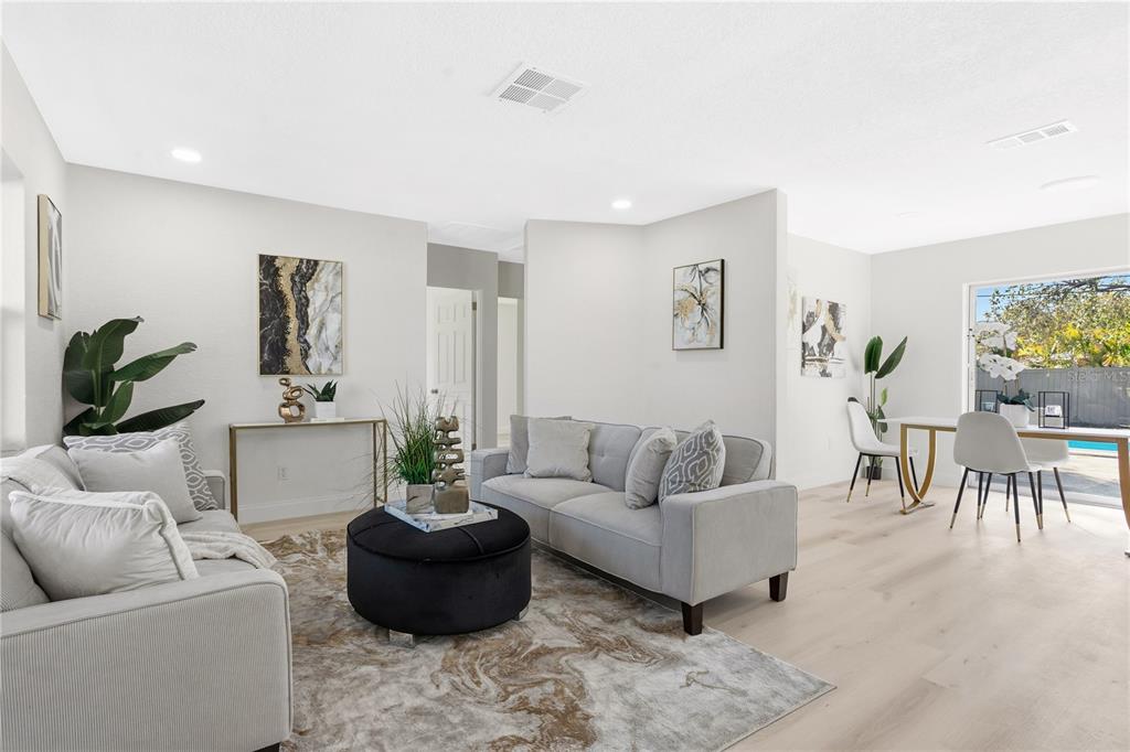 A living room with light wood floors, grey sofas, a black ottoman, and dining area — 214 45TH AVENUE NE, ST PETERSBURG, FL