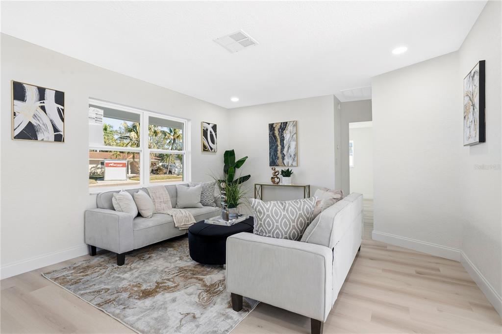 A living room features light wood flooring, a gray sofa, and a dark circular ottoman — 214 45TH AVENUE NE, ST PETERSBURG, FL