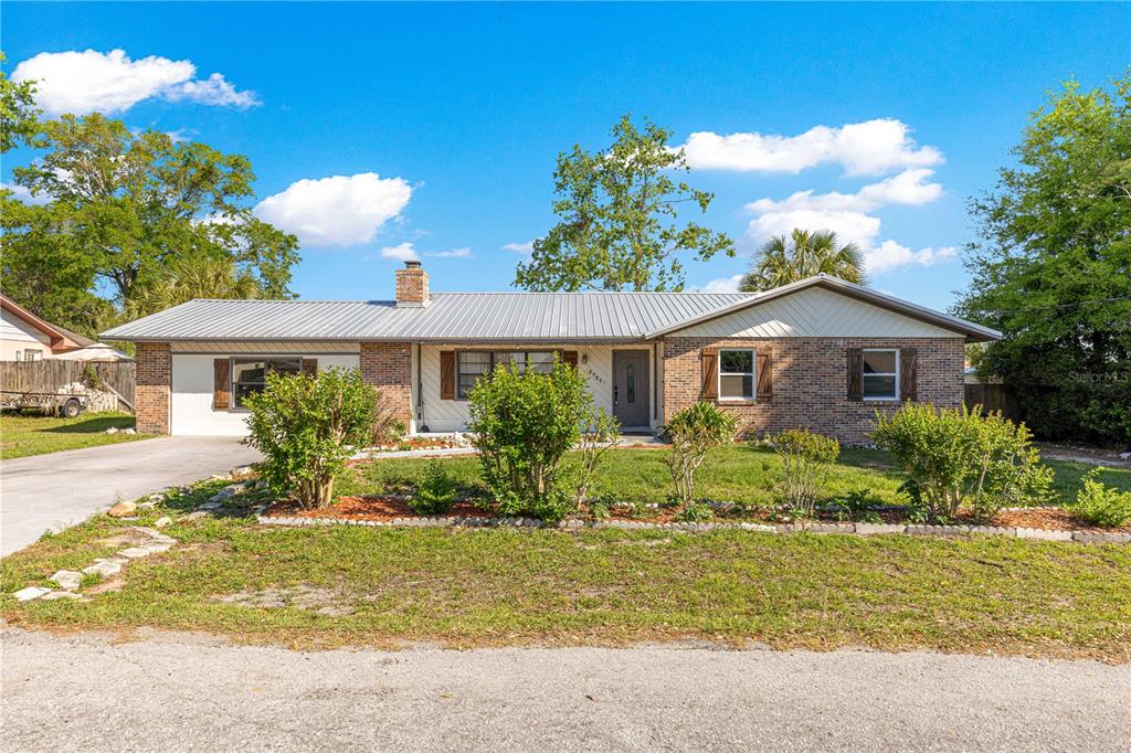 A single-story brick house with a metal roof, front yard landscaping, and a concrete driveway — 5721 SE 21ST LANE, OCALA, FL