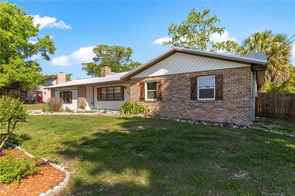 A single-story brick house with a metal roof and wooden shutters sits on a lawn — 5721 SE 21ST LANE, OCALA, FL