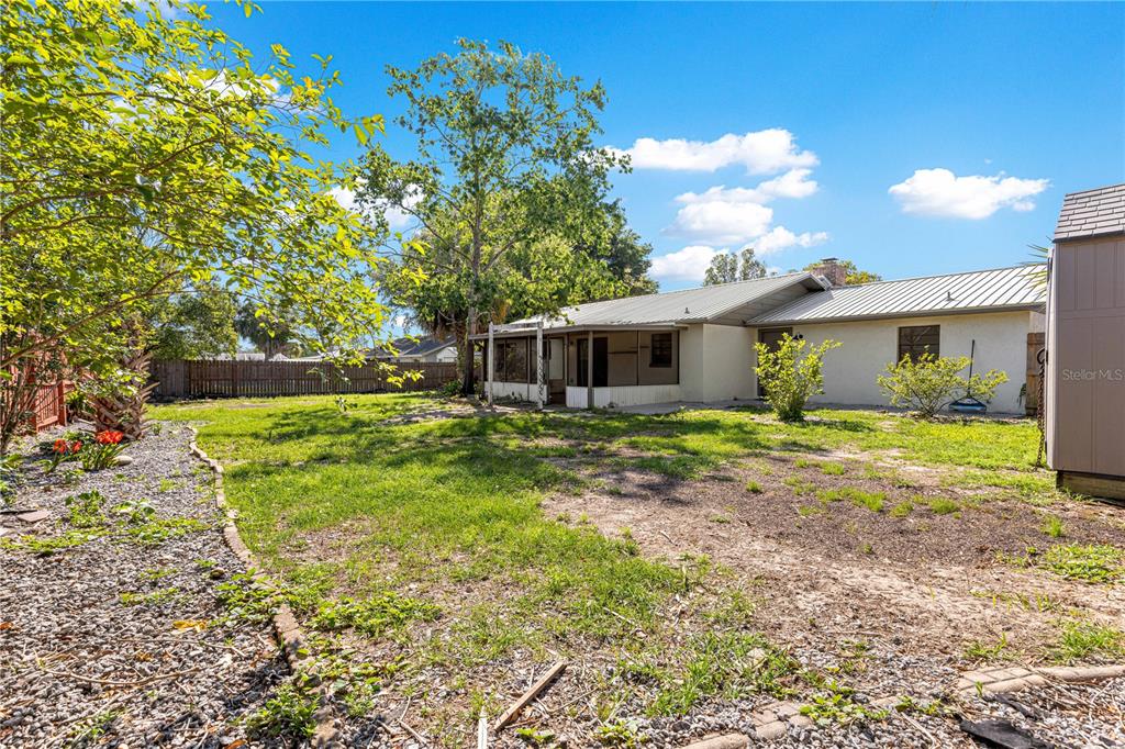 A backyard view of a single-story house with a metal roof and a screened porch — 5721 SE 21ST LANE, OCALA, FL