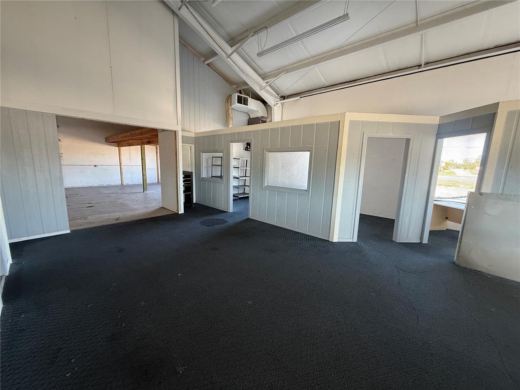 An interior view shows a carpeted room with gray paneled walls, windows, and doorways — 3060 PLACIDA ROAD, ENGLEWOOD, FL