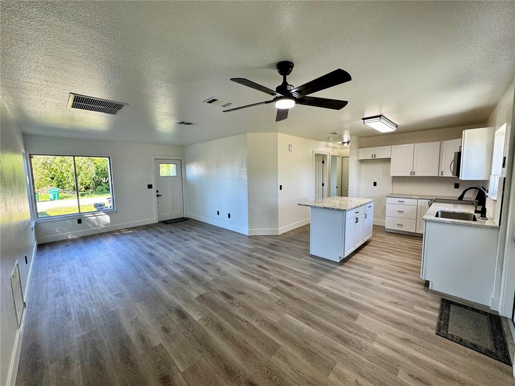 An open-concept living area features light wood-look flooring, a kitchen island, and white cabinetry — 325 CAPATOLA ST, PORT CHARLOTTE, FL