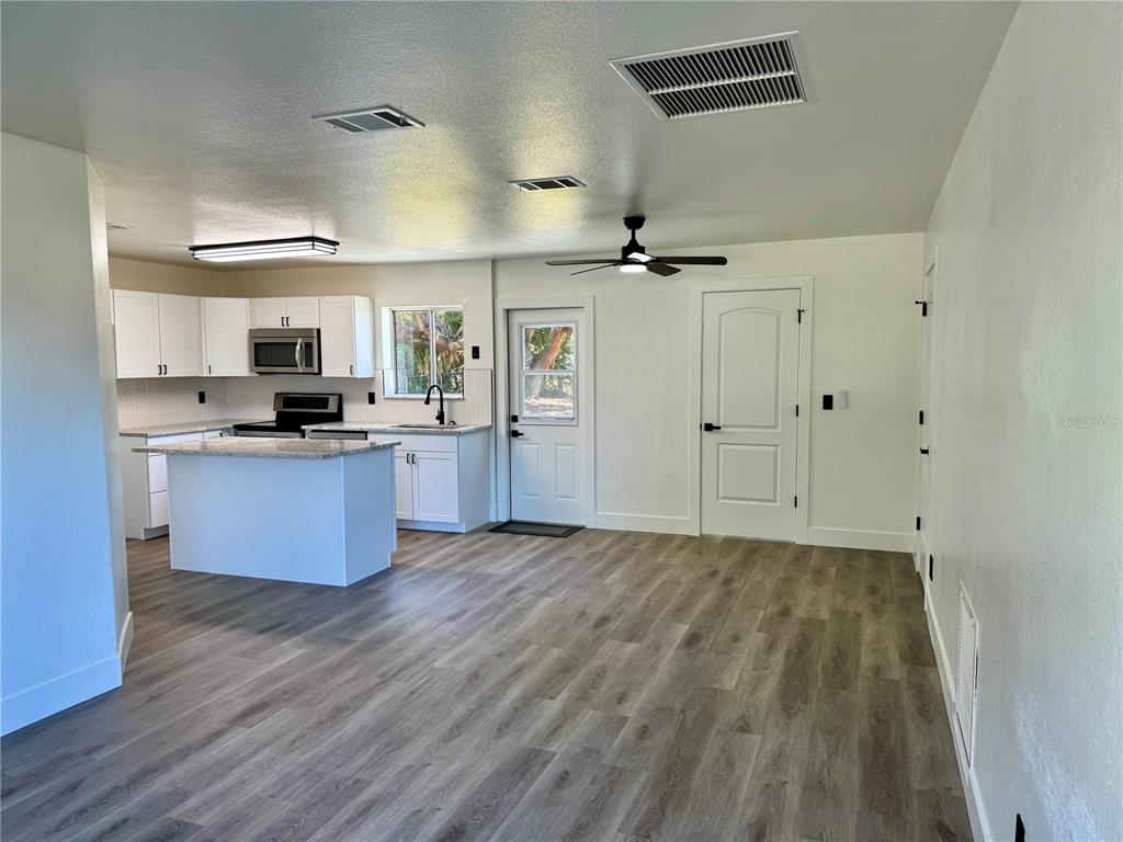 A kitchen with white cabinets and a center island opens into a living area — 325 CAPATOLA ST, PORT CHARLOTTE, FL