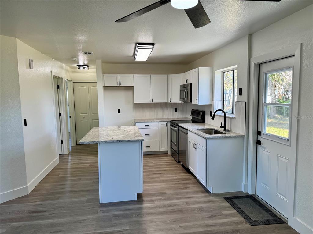 A kitchen features white cabinets, granite countertops, stainless steel appliances, and light wood-look flooring — 325 CAPATOLA ST, PORT CHARLOTTE, FL