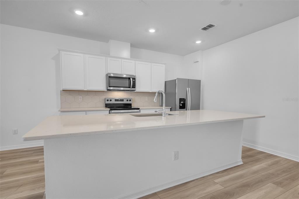 A modern kitchen features white cabinetry, stainless steel appliances, a quartz island, and light flooring — 11398 NONA SOUND STREET, ORLANDO, FL