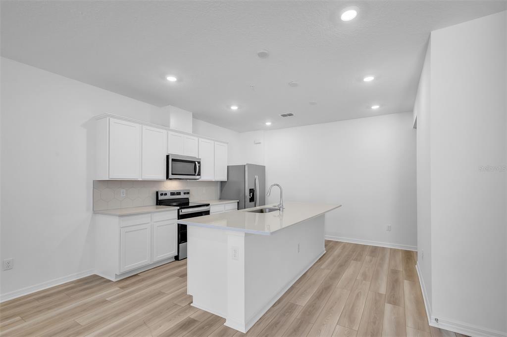 A modern kitchen features white cabinets, stainless steel appliances, and a central island with seating — 11398 NONA SOUND STREET, ORLANDO, FL