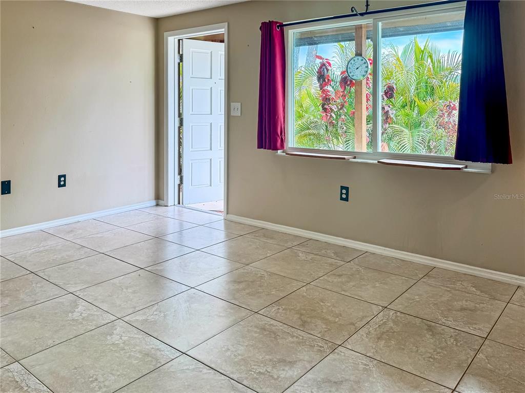 A room with beige tile flooring, a white door, and a window with purple curtains — 934 FUNDY ROAD, VENICE, FL