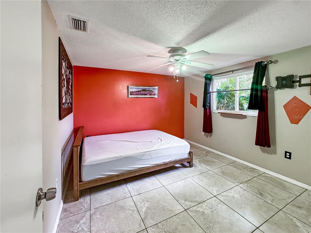 A bedroom features a bed against a red accent wall, tile flooring, and a window — 934 FUNDY ROAD, VENICE, FL