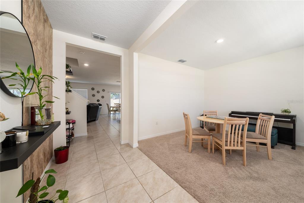 A dining area with carpeted flooring and a piano sits adjacent to a tiled hallway — 2824 BIG SUR ROAD, DAVENPORT, FL
