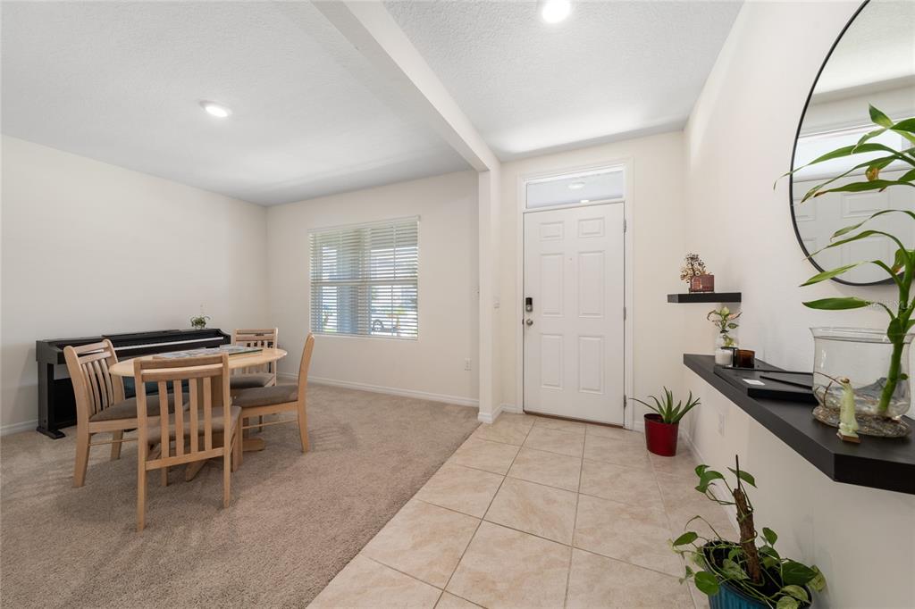 A room with a tiled entryway, carpeted dining area, piano, and a white front door — 2824 BIG SUR ROAD, DAVENPORT, FL