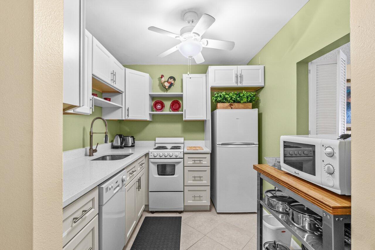 A small kitchen features white cabinets, light green walls, a white stove, and a refrigerator — 68 Suffolk B # 68, Boca Raton FL 33434, BOCA RATON, FL