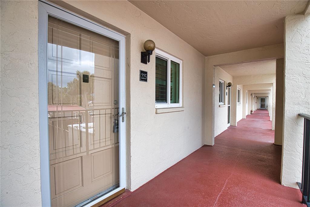 An exterior walkway with red flooring leads past a series of apartment doors and windows — 240 SANTA MARIA STREET UNIT 225, VENICE, FL