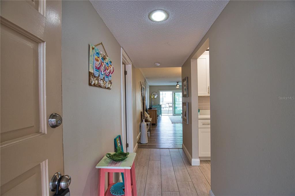 A hallway with tile flooring leads from an entryway toward a bright living area — 240 SANTA MARIA STREET UNIT 225, VENICE, FL