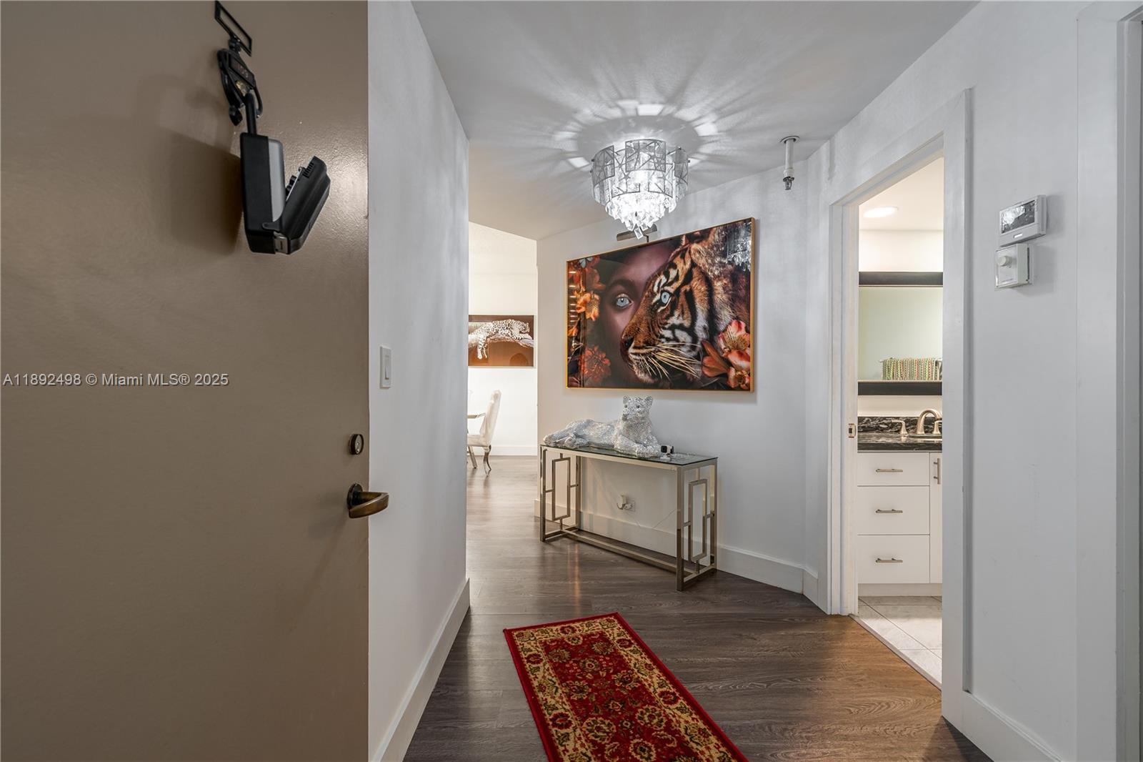 An entryway features a tiger-themed painting, a crystal chandelier, and a red runner rug — 7300 Radice Ct # 109, Lauderhill FL 33319, LAUDERHILL, FL