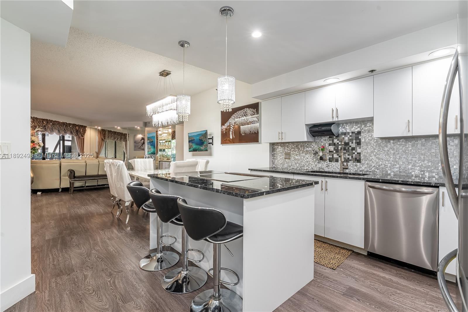 A modern kitchen features white cabinetry, a black granite island, and bar stools — 7300 Radice Ct # 109, Lauderhill FL 33319, LAUDERHILL, FL