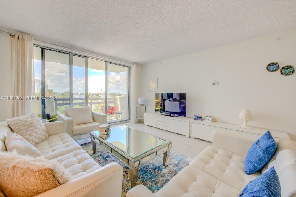 A bright living room features white tufted sofas, a glass coffee table, and balcony views — 1500 Bay Rd # 528S, Miami Beach FL 33139, MIAMI BEACH, FL