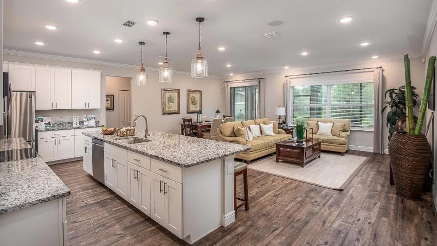 An open-concept kitchen with granite countertops and white cabinets overlooks a living and dining area — 7726 105th Avenue, Vero Beach FL 32967, VERO BEACH, FL