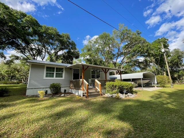 A single-story house with light gray siding features a covered front porch and a carport — 20911 NE 142ND PLACE, FORT MC COY, FL