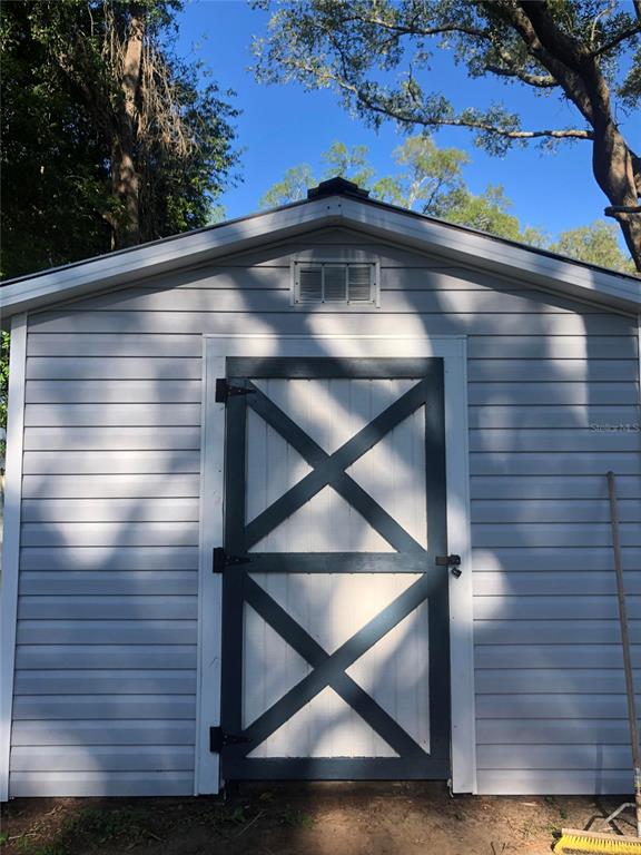 A light gray vinyl-sided shed features a dark-trimmed door with an X-pattern design — 20911 NE 142ND PLACE, FORT MC COY, FL