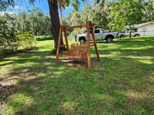 A wooden swing set sits on a grassy lawn in front of a parked pickup truck — 20911 NE 142ND PLACE, FORT MC COY, FL