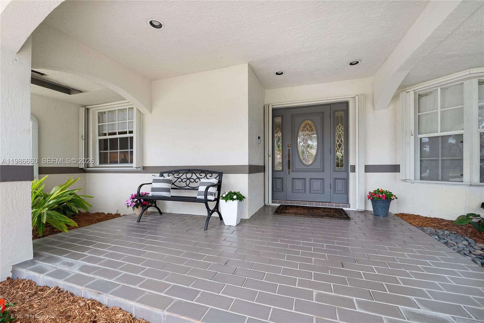 A covered porch features gray tiled flooring, a black metal bench, and a gray front door — 10422 SW 121st St, Miami FL 33176, MIAMI, FL