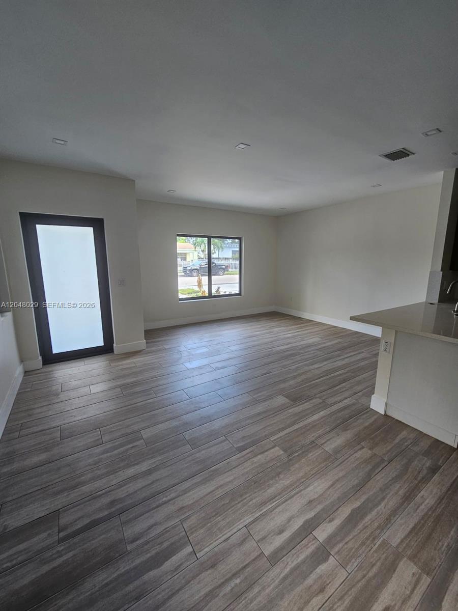 This open-concept living area features wood-look tile flooring, recessed lighting, and a glass-paneled door — 5428 NW 3rd Ave # B, Miami FL 33127, MIAMI, FL