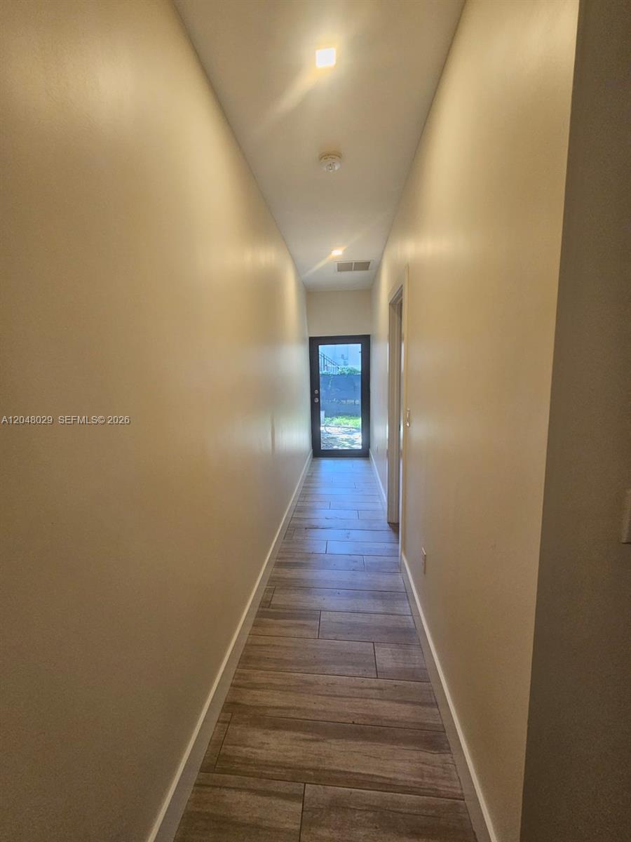 A narrow hallway features light-colored walls, wood-look tile flooring, and a glass-paneled exterior door — 5428 NW 3rd Ave # B, Miami FL 33127, MIAMI, FL