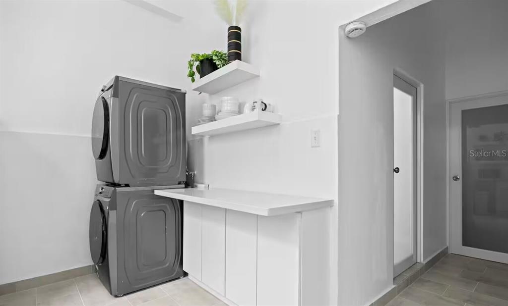 A laundry room features stacked gray appliances, white cabinetry, and open shelving against white walls — 250 CALLE DEL PARQUE UNIT 3B, SAN JUAN, PR