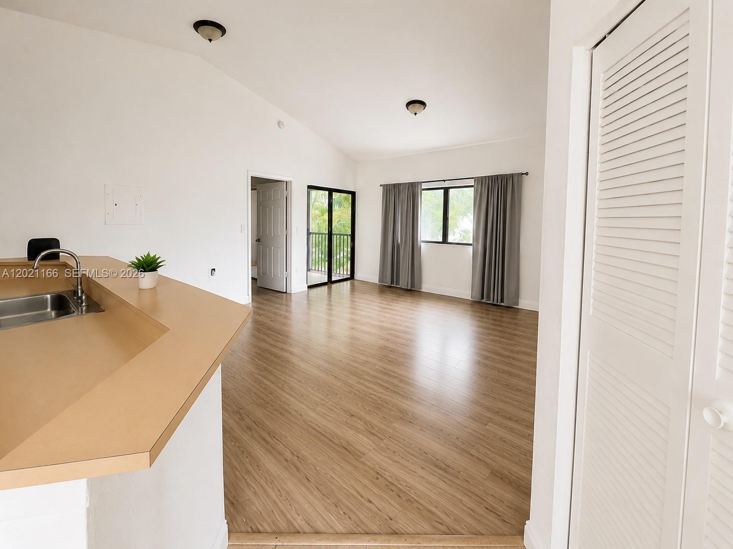 A kitchen counter overlooks an empty living area with wood-look flooring and a balcony door — FORT LAUDERDALE, FL